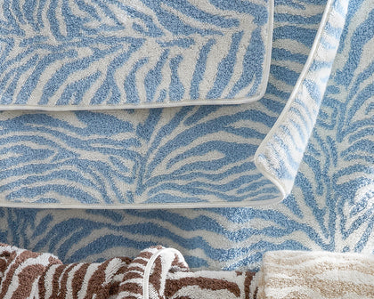 Blue zebra-print Regine towels stacked beside brown and taupe towels.