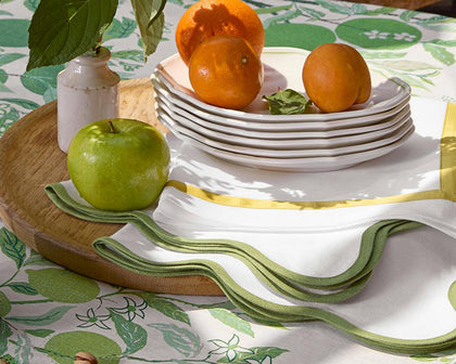 White Scallop Edge napkins with green wavy trim on a citrus-print tablecloth, stacked plates with fruit.