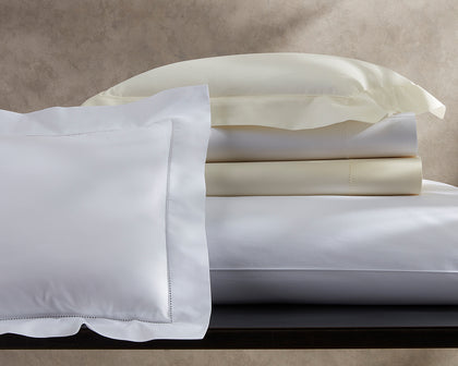 White and cream Sierra Hemstitch sheets and pillow shams stacked together on a console.