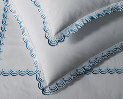 White Stella bedding with blue scalloped embroidered trim styled on a bed.