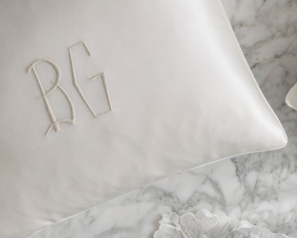 White monogrammed silk pillowcase from The Silk Collection on a marble surface with lace fabric.