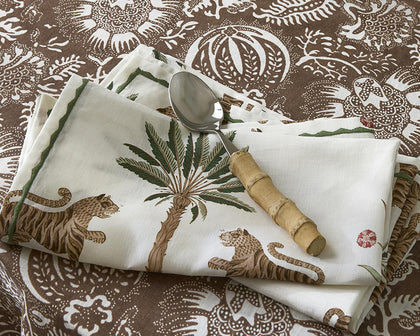 White Tiger Palm napkin with tiger and palm print on a brown paisley tablecloth with a bamboo-handled spoon.