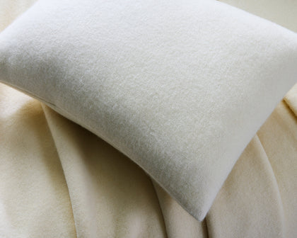 Cream Venus wool blanket and matching pillow on a bed.