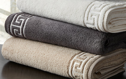 Stack of ivory, charcoal, and tan Adelphi towels with geometric border embroidery