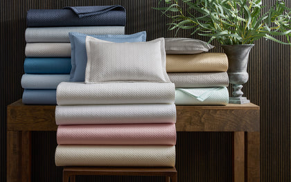 Alba textured pique bedding stacked in an array of pastel colors, near a potted plant.