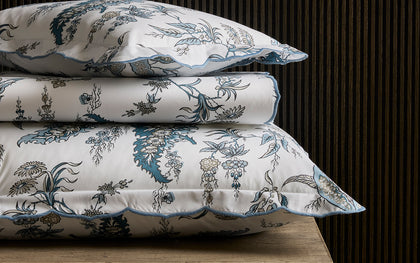 Blue Apolline floral print scalloped bedding, stacked on a wooden table.