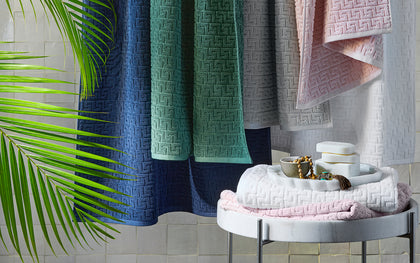 Athena greek-key textured towels in navy, green, gray, and pink, hung over a rail.
