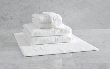 White Auberge monogrammed towels and bath mat stacked on marble tile.