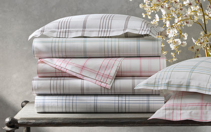 White August Plaid sheets in gray, green, pink, and blue, stacked beside cherry blossoms.