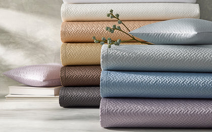 Basketweave quilted bedding stacked in an array of colors, beside a sprig of dried berries.