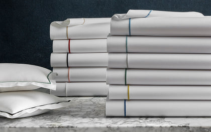 White Bergamo sheets stacked with a rainbow of trim colors, on a marble table.