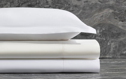 Stacked white Bergamo Hemstitch sheets with hemstitch trim against a marble backdrop.