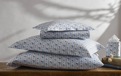 Blue and white Cabanon Stripe floral bedding stacked on a wooden table.