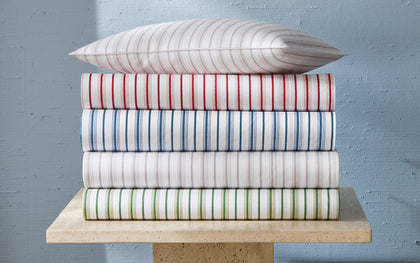 White Calypso striped sheets in assorted colors, stacked with a matching pillow.