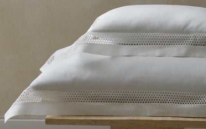White Cecily pillows with lattice lace trim, stacked on a stone bench.