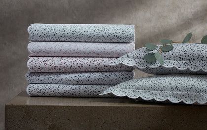 Celine speckled-print scalloped bedding in green, red, and black, stacked beside eucalyptus.
