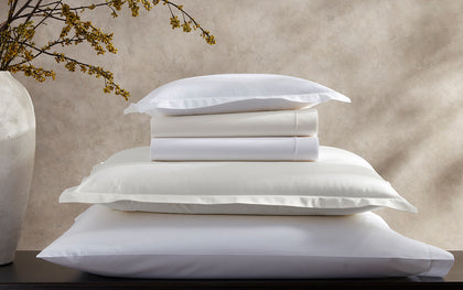 White and ivory Ceylon Satin Stitch pillows stacked, beside a flowering branch.