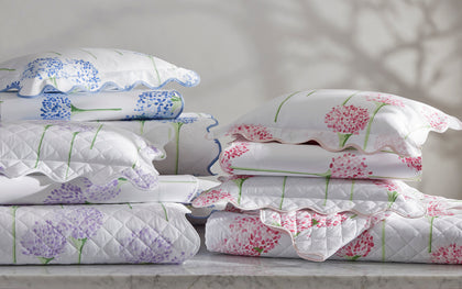 Charlotte floral quilted shams in pink, purple, and blue, stacked on a marble table.