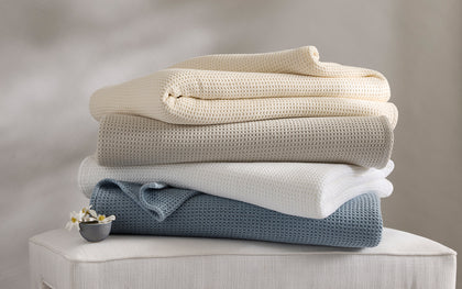 Waffle-weave Chatham blankets in tan, ivory, and white, folded and draped on a bed.