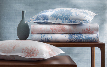Chrysanthemum print bedding in blue and pink, stacked with matching pillows on nesting tables.