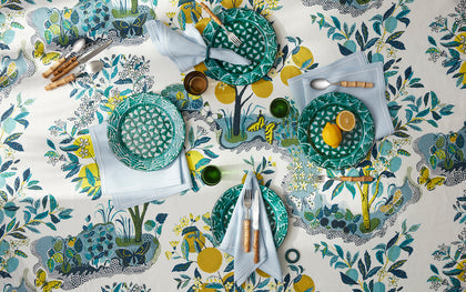 Citrus Garden print tablecloth with lemon trees, set with green textured plates and blue napkins.