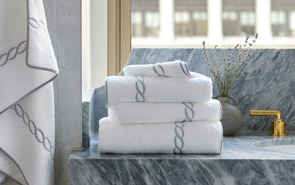 White Classic Chain towels with chain-link embroidered trim, stacked on a marble vanity.