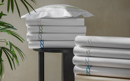 White Classic Chain sheets stacked with chain-link embroidered trim in assorted colors, near a plant.