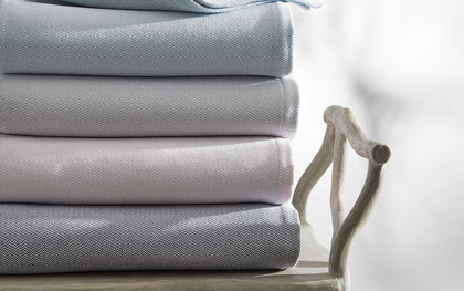 Costa Mesa textured blankets in pale blue, gray, and pink, stacked on a chair.