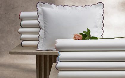 White Dakota scalloped sheets stacked with colorful edge trim, topped with a pink rose.