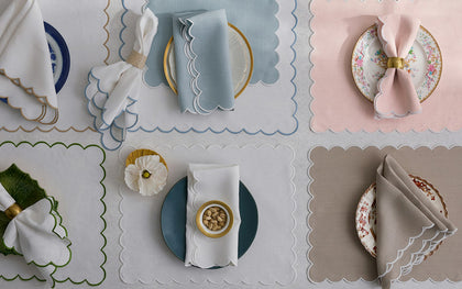 Dakota scalloped placemats in blue, pink, white, and tan, each set with a plate and napkin.