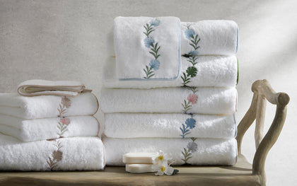 Daphne embroidered towels stacked on a wooden bench with a fresh flower