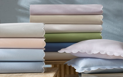 Diamond Pique scalloped sheets in pastel colors, stacked with matching pillows on side tables.