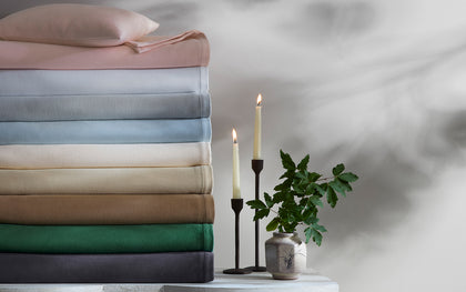 Dream Modal sheets stacked in a rainbow of solid colors, beside candles and greenery.
