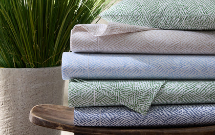 Duma Diamond print sheets in green, tan, blue, and navy, stacked on a wooden stool.