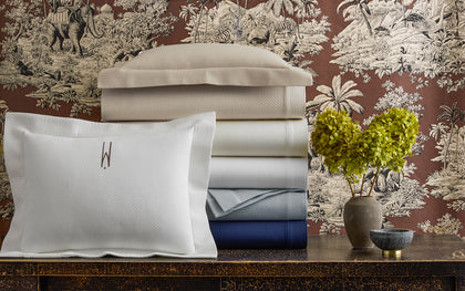 White Elliot textured pique bedding stacked in ivory, gray, and navy, beside a monogrammed pillow.