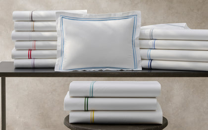 White Essex bedding stacked with multicolor contrast stitching and a blue bordered pillow sham.