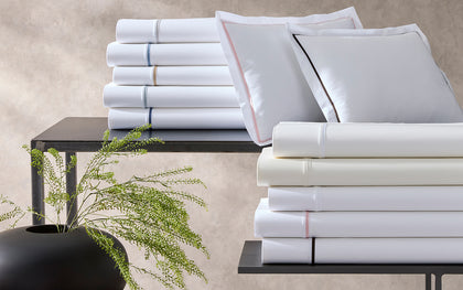 White Gatsby bedding stacked with contrast piping in various colors and pillow shams with pink and black trim.