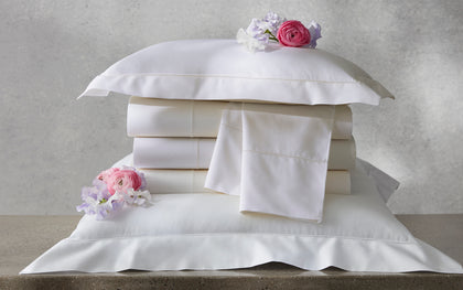 Ivory Gatsby hemstitch bedding stacked with pillow shams and fresh flowers.
