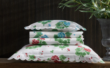 White Geranium print bedding stacked with scalloped edges in blue and red floral patterns.