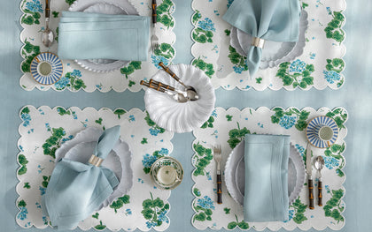 White and blue Geranium print placemats set with blue napkins and white plates, seen from above.
