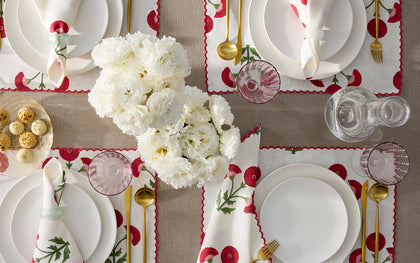 White Gisele placemats embroidered with red poppies, set with white plates and gold flatware, seen from above.