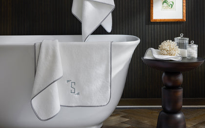 White Giza cotton towels with a grey monogram draped over a clawfoot tub