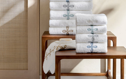 White Gordian Knot towels stacked with embroidered knot borders in blue and gold, on a wooden table.