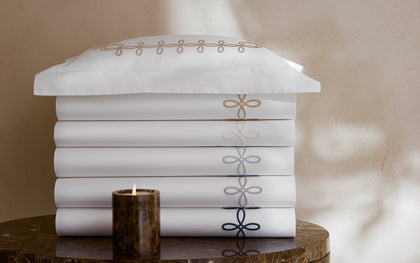White Gordian Knot bedding stacked with an embroidered border in shades of gold, gray, and navy.