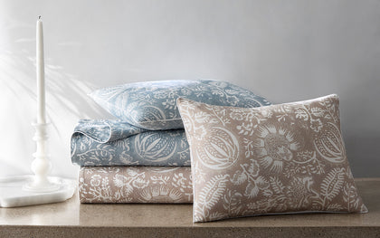 Granada floral print sheets and a sham in blue and tan, stacked on a stone surface.