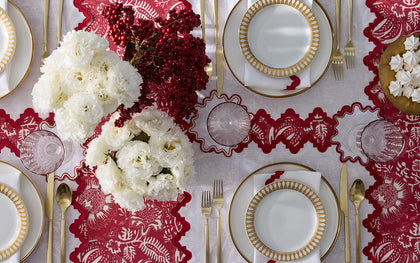 Red Granada floral print scalloped placemats set with gold-rimmed china, white ranunculus, and berries.