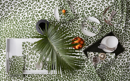 Green Iconic Leopard print tablecloth and napkins set with white plates, a palm frond, and apricots.