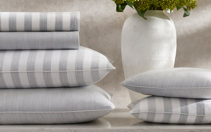 Lana grey striped sheets and pillows stacked beside a vase