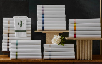 White Lowell sheets stacked with ribbon trim in a rainbow of colors, one monogrammed.