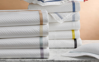 White Lowell Matelasse quilted shams stacked with ribbon trim in assorted colors, beside red berries.